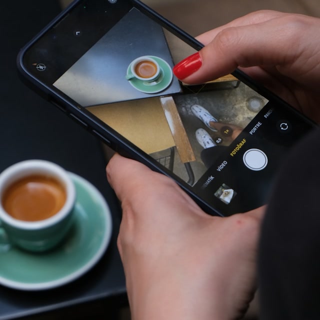 A Nyoo Studio hospitality post in the making: a phone photographing an espresso on a café table, in the studio's amber duotone.